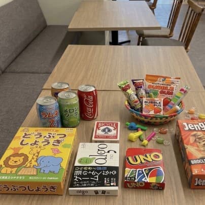 テーブルに並んだボードゲーム(どうぶつしょうぎ、algo、UNO、ジェンガ、トランプ)と缶ジュース、かごに入ったお菓子の写真