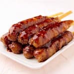 白い皿に盛られた、タレのかかった串付きの肉巻きおにぎり