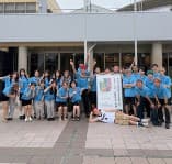 建物の前で集合写真を撮る、水色のTシャツ姿のバスケットボール部の部員たち
