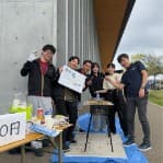 屋外の模擬店で焼き台を囲んでポーズをとる部員たち