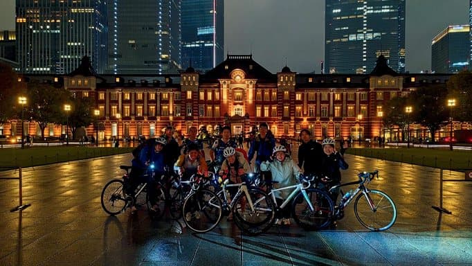 夜の駅舎の前に自転車と並ぶツーリング部の部員の集合写真