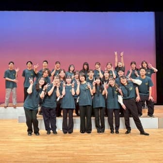 ステージ上でそろいのTシャツを着てポーズをとる軽音楽部の集合写真
